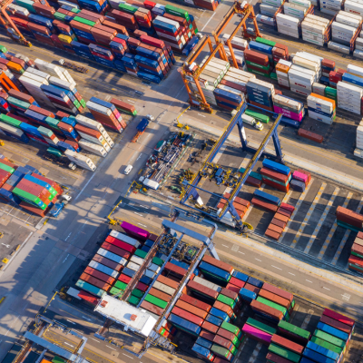 Luftaufnahme von gestapelten Schiffscontainern und Kränen in einem geschäftigen Hafenterminal.