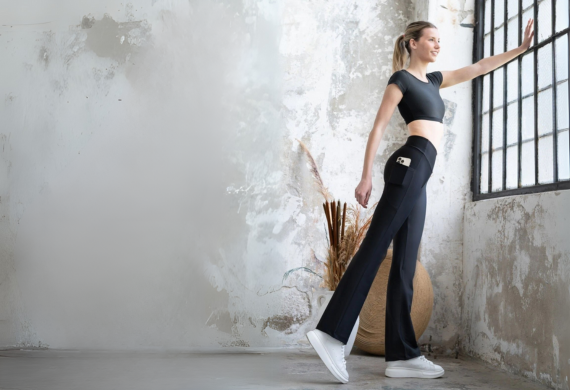 Frau in Sportkleidung streckt sich an einem Fenster in einem minimalistischen, rustikalen Raum.