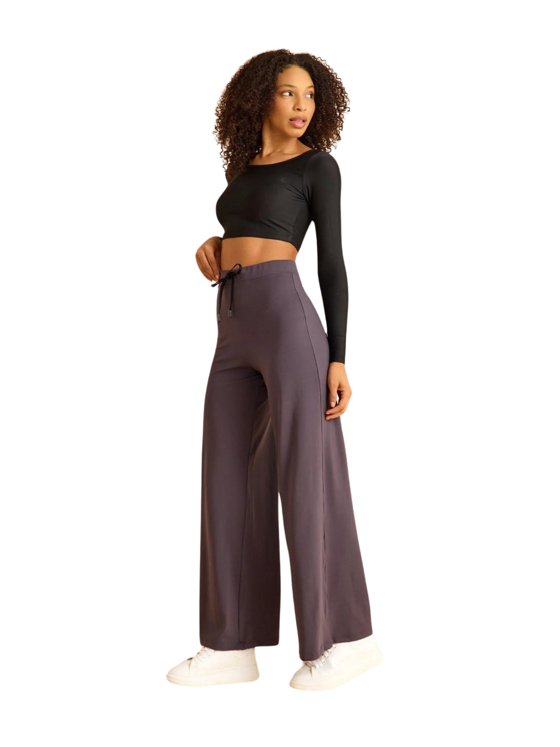 Frau in schwarzem Crop-Top und Lismina 446 Mumbai Yoga Hose in Anthrazit, seitlich posierend in vielseitigen weißen Sneakers.