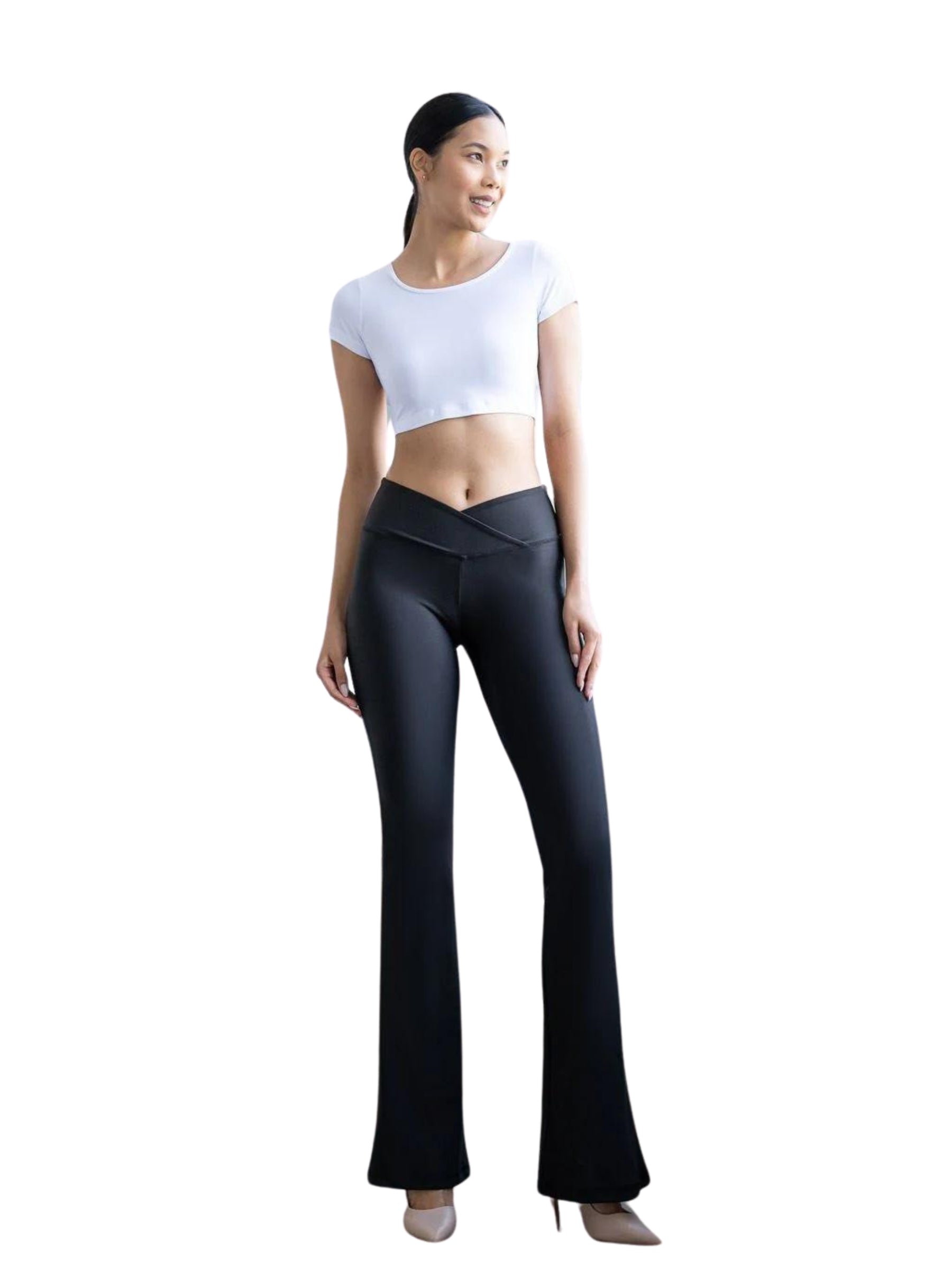 Frau in Lisminas 438 Scrunch Butt Leggings in Schwarz, weißem bauchfreiem Top und beigen Heels vor einem schlichten Hintergrund.