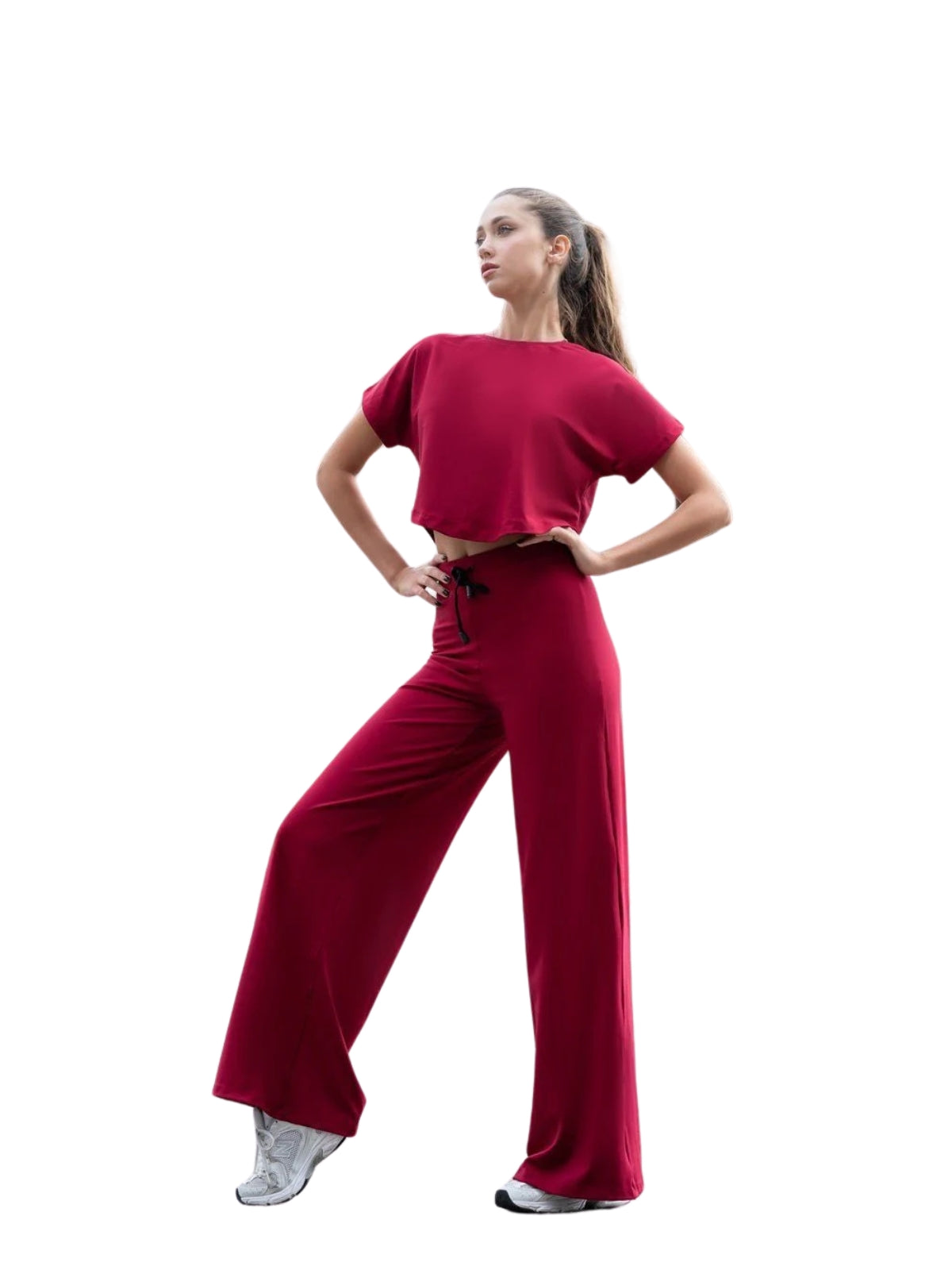 Eine Person in einem Lismina 097 Yoga T-Shirt in Bordeaux, Schlaghosen und weißen Sneakers steht selbstbewusst vor einem weißen Hintergrund.