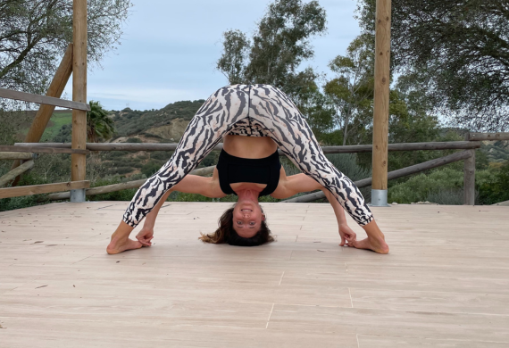 Person in Leggings mit Tiermuster, die im Freien eine Yoga-Pose mit weit gespreizten Beinen und Vorwärtsbeuge macht.