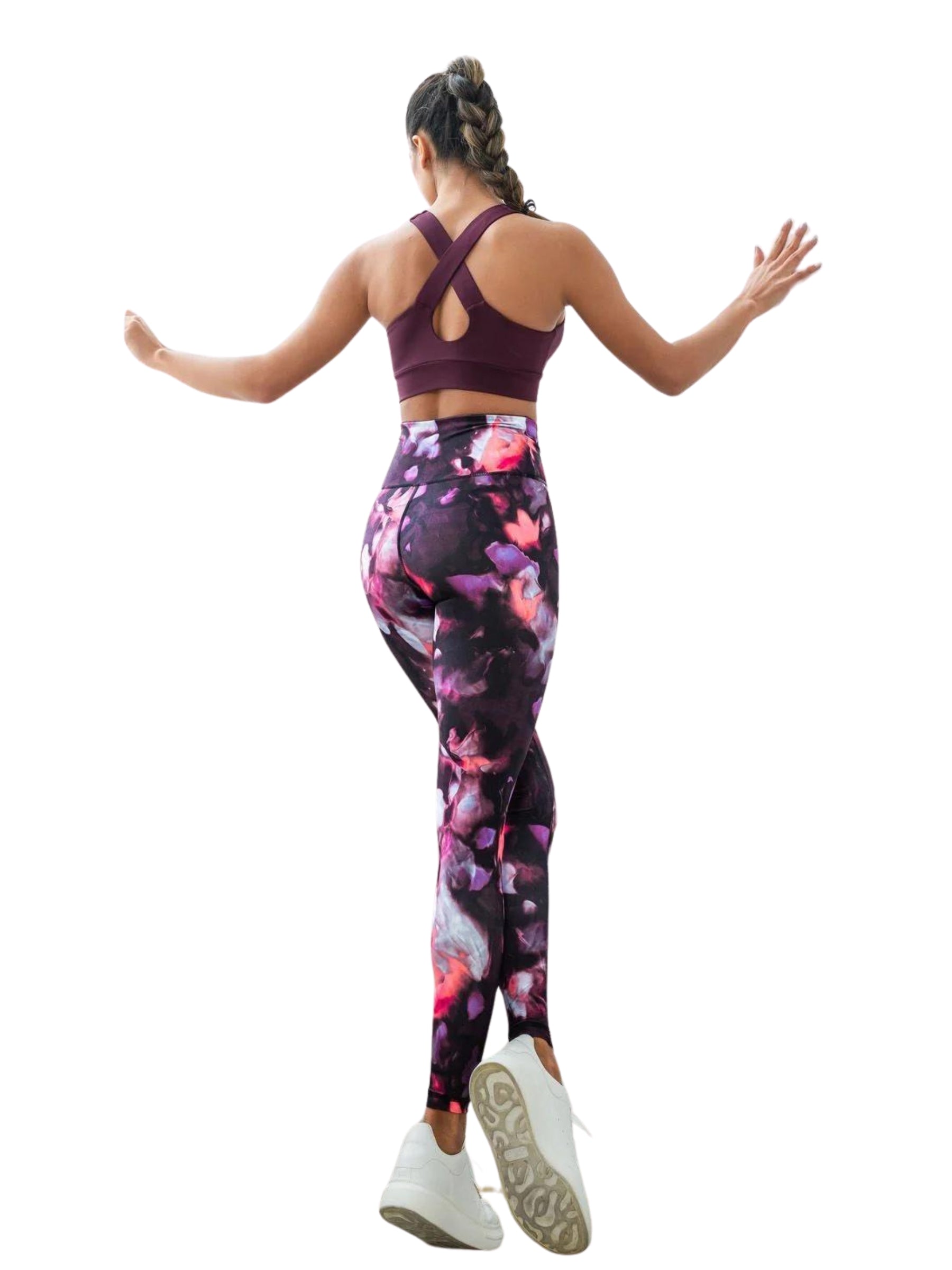 Person in Lisminas rosa-schwarzen Leggings mit hoher Taille und kastanienbraunem Sport-BH, geflochtenes Haar, springt vor einem weißen Hintergrund.