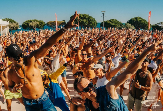 Eine große Menschenmenge genießt draußen einen sonnigen Tag, viele Leute nehmen eine spielerische Tupfpose ein.
