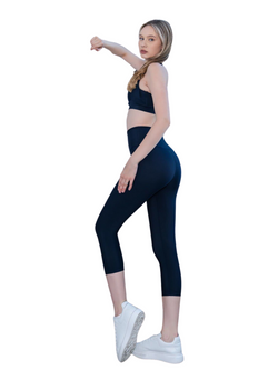 Frau in Lisminas 947 Capri-Leggings in Marineblau und weißen Turnschuhen posiert in Seitenansicht vor einem weißen Hintergrund.