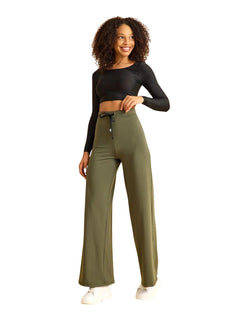Person in einem schwarzen bauchfreien Top, einer Lismina 450 Mumbai Yoga-Hose in Khaki und weißen Turnschuhen vor einem weißen Hintergrund.