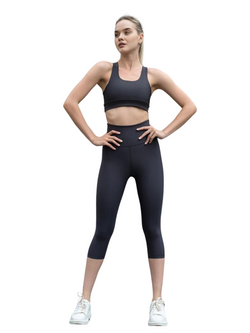 Eine Person in Lisminas 944 Capri Leggings in Antrazit und weißen Sneakers steht selbstbewusst da, die Hände in die Hüften gestemmt.