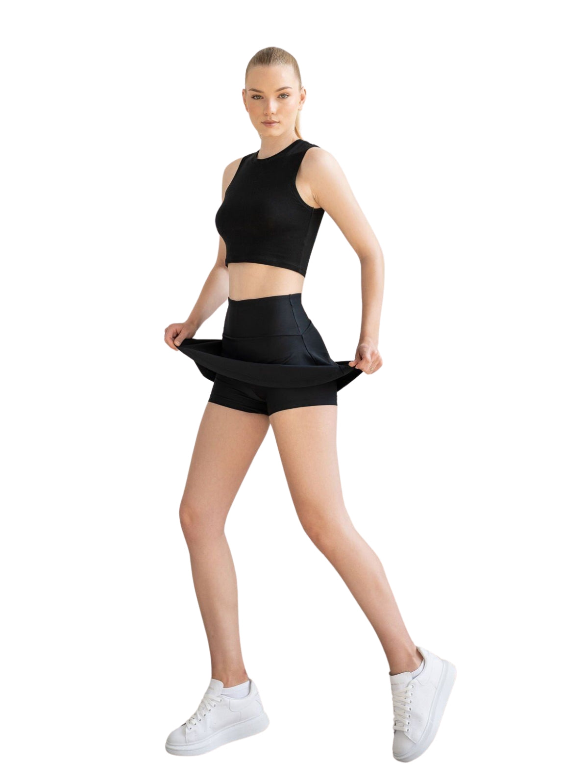 Frau in Lismina 440 Rock in Schwarz und Crop Top, posiert in weißen Turnschuhen vor einem weißen Hintergrund.