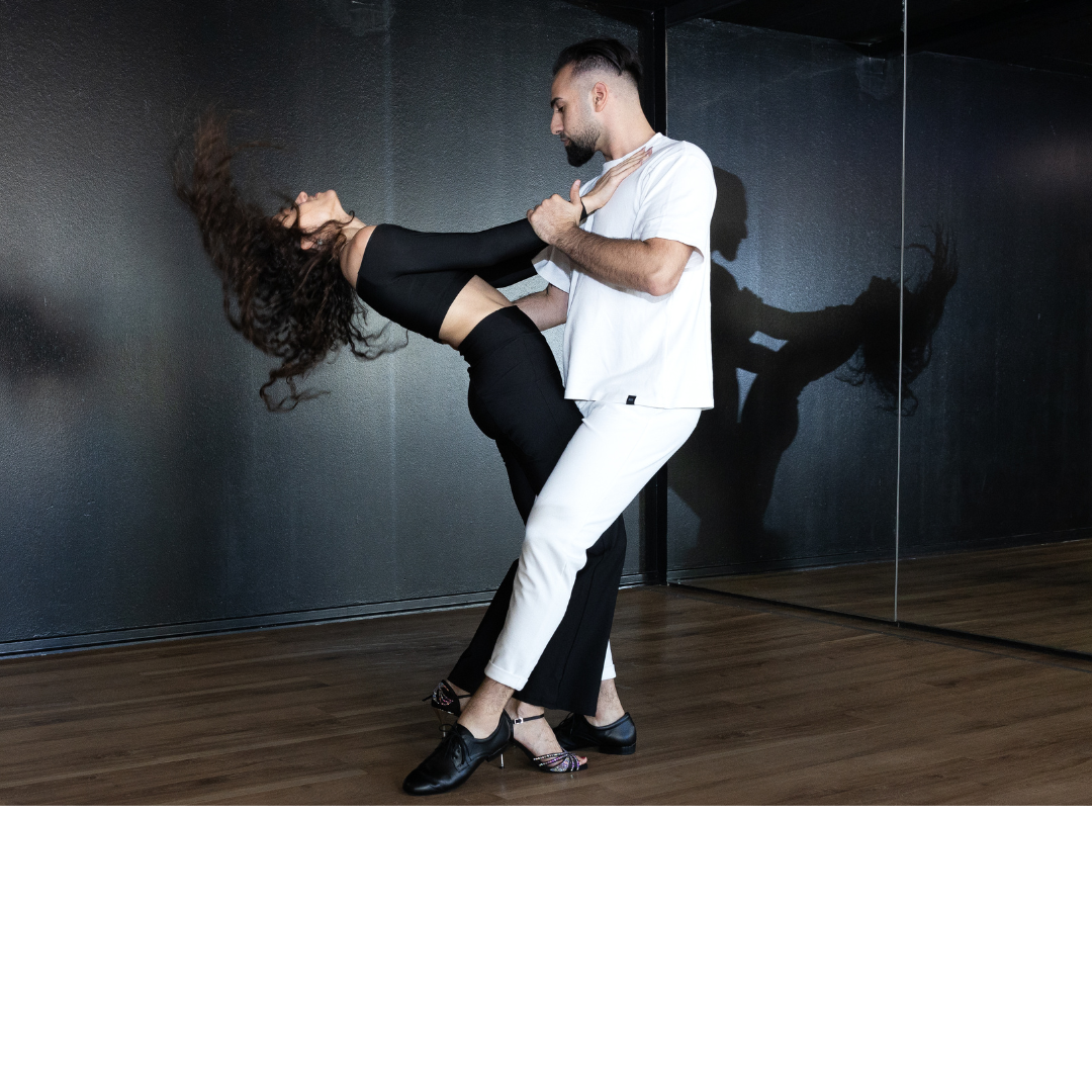 Tanzpartner tauchen anmutig in ein Studio ein und werfen dabei ein Spiegelbild auf eine verspiegelte Wand.