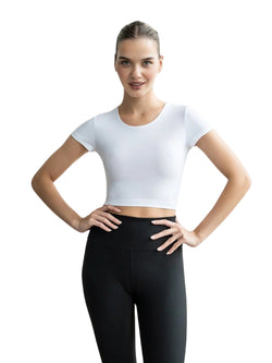 Frau in einem Lismina 094 Larissa Sport Top in Weiss und schwarzen Leggings, Hände in die Hüften gestemmt, lächelt vor einem schlichten Hintergrund.