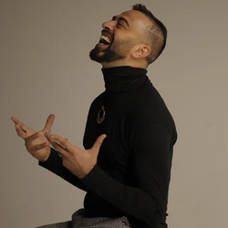 Lachender Mann in einem schwarzen Rollkragenpullover von Tanzkurse sitzt im Salsa-Rhythmus vor der Kulisse von The Backyard.