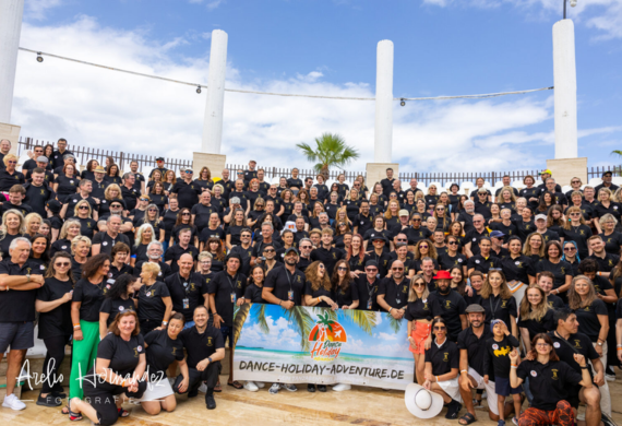Großes Gruppenfoto mit lächelnden Menschen in schwarzen Hemden, die im Freien ein Banner halten.