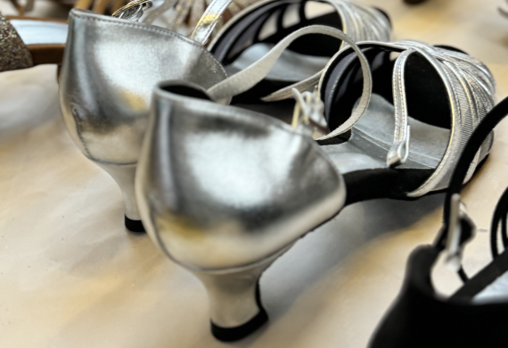 Ein Paar silberne, riemenförmige, niedrighackige Tanzschuhe auf einer hellen Oberfläche.