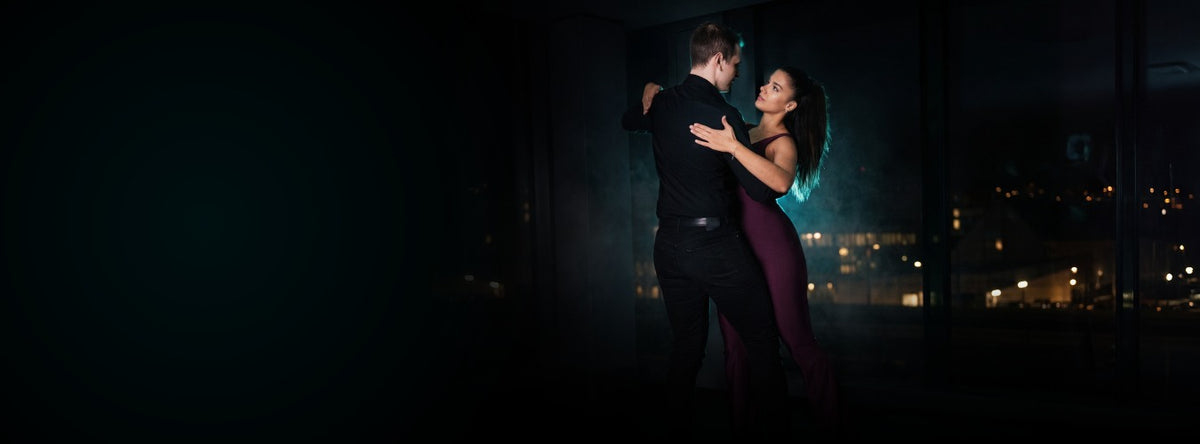 Tanzpaar in Schwarz und Bordeaux im dunklen Studio, Stadtlichter im Hintergrund
