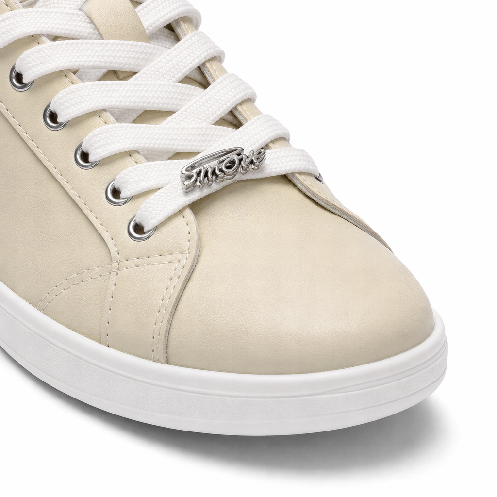 Nahaufnahme des „Dancing Queens SMOVE Accent Dance Sneaker“ in Creme für Damen mit weißen Schnürsenkeln und einem metallischen Anhänger.