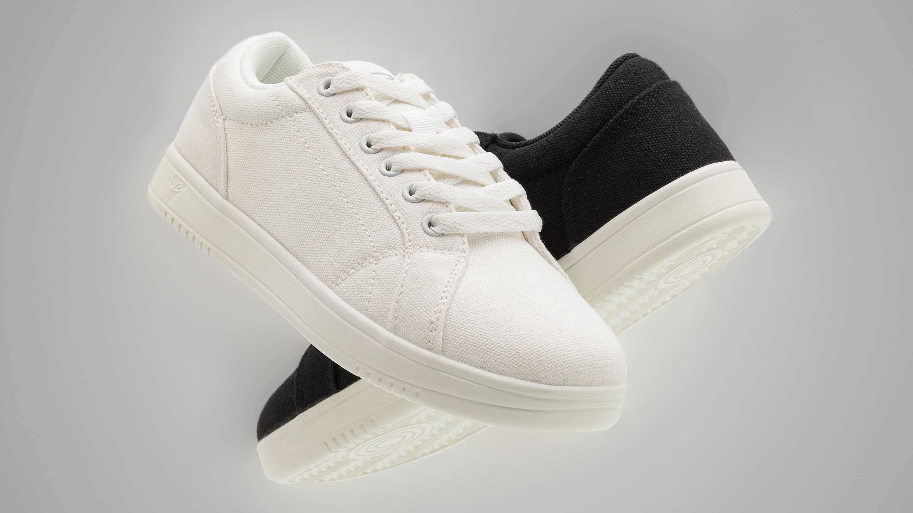 Ein Paar weiß-schwarze Turnschuhe mit weißen Sohlen, die vor einem grauen Hintergrund schweben.