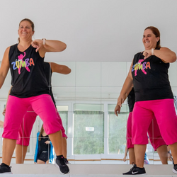 Ein Zumba-Fitnesstrainer in Passion to Dance-Kleidung von Tanzkurse tanzt energisch in einem verspiegelten Studio.