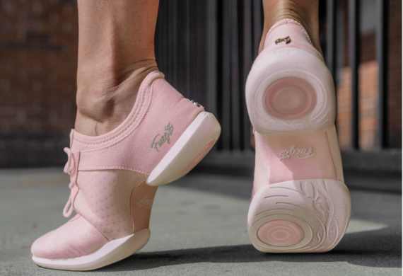 Rosa Turnschuhe mit weißen Sohlen, die von einer Person getragen werden, wobei ein Fuß auf einer Betonoberfläche angehoben ist und das Sohlendesign sichtbar ist.