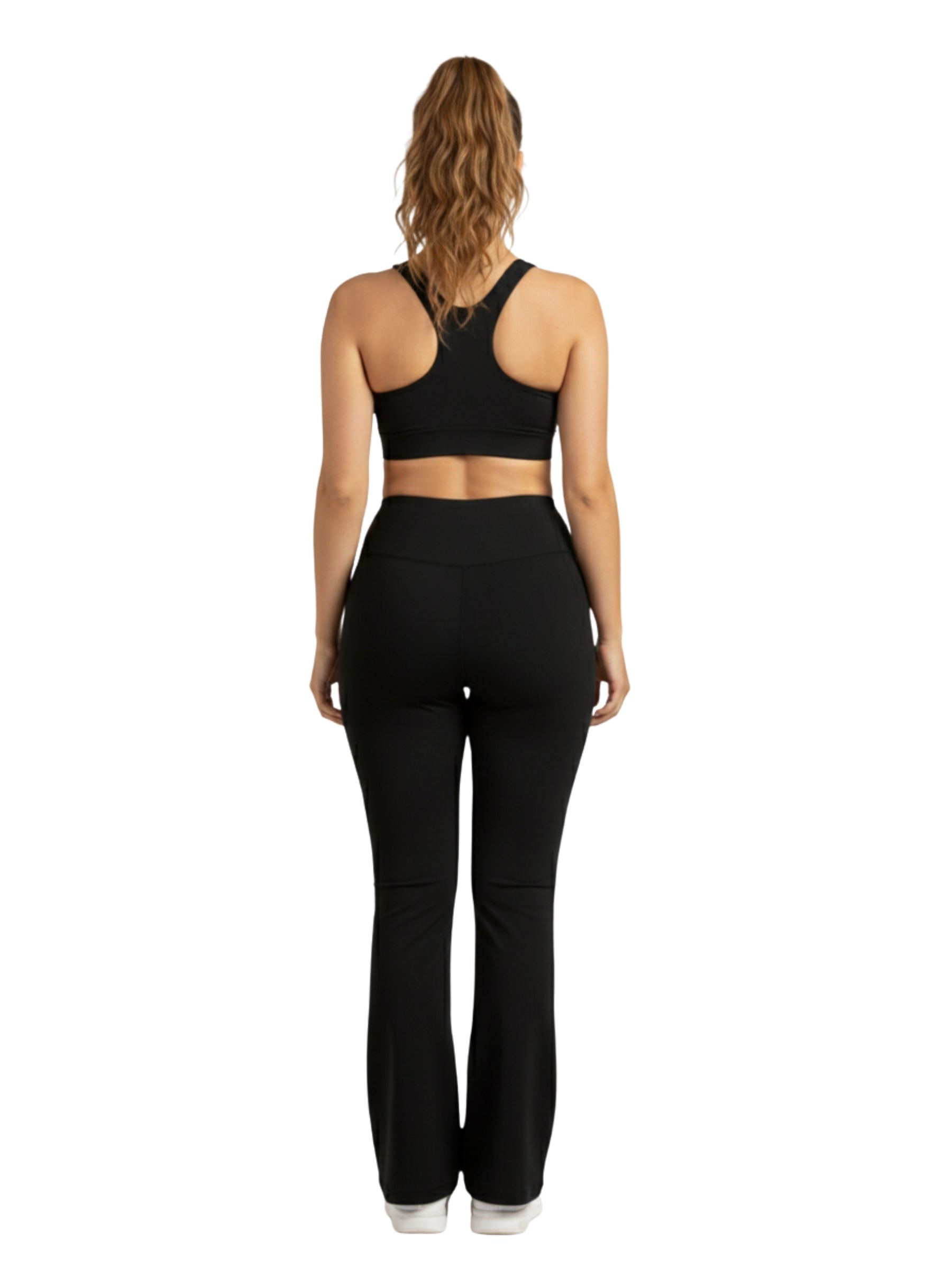 Frau in schwarzem Sport-BH und Dancing Queens Luna Flare Pocket Leggings in Schwarz steht mit dem Rücken zur Wand.