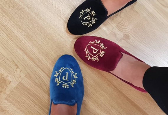 Drei Paar bestickte Slipper in Blau, Rot und Schwarz auf einem Holzboden.