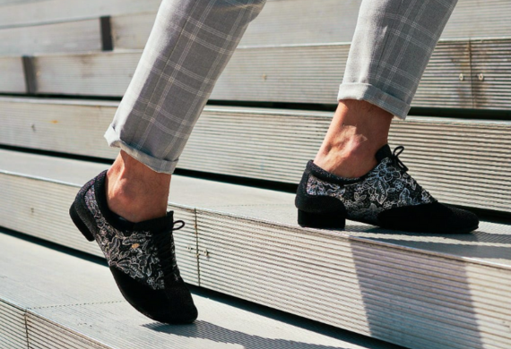 Person in karierten Hosen geht mit gemusterten schwarzen Abendschuhen eine Treppe hinauf.