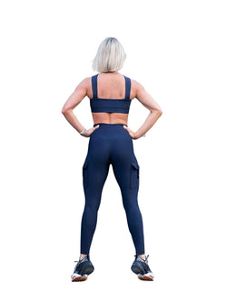 Eine Person mit kurzen Haaren steht mit den Händen auf den Hüften in Lisminas 1141 Leggings mit Taschen in Marineblau und betont die hohe Taille.