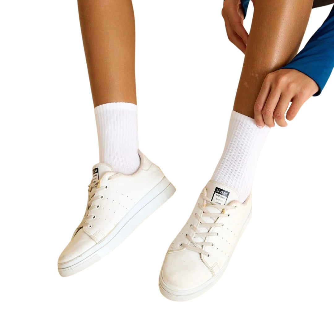 Eine Person in einem blauen Sport- und Tanzoutfit passt ihre Lismina 455-4 Socken in Weiss zu weißen Sneakers an.