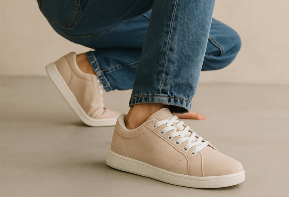 Person in hellbeigen Turnschuhen und blauen Jeans, die auf einem glatten, hellen Boden hockt.