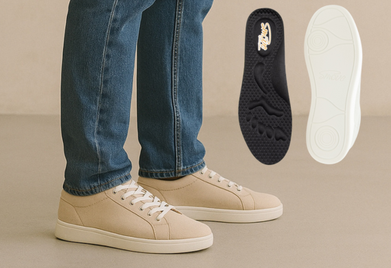 Person in beigen Turnschuhen mit weißen Sohlen und Schnürsenkeln; rechts daneben zwei Einlegesohlen.