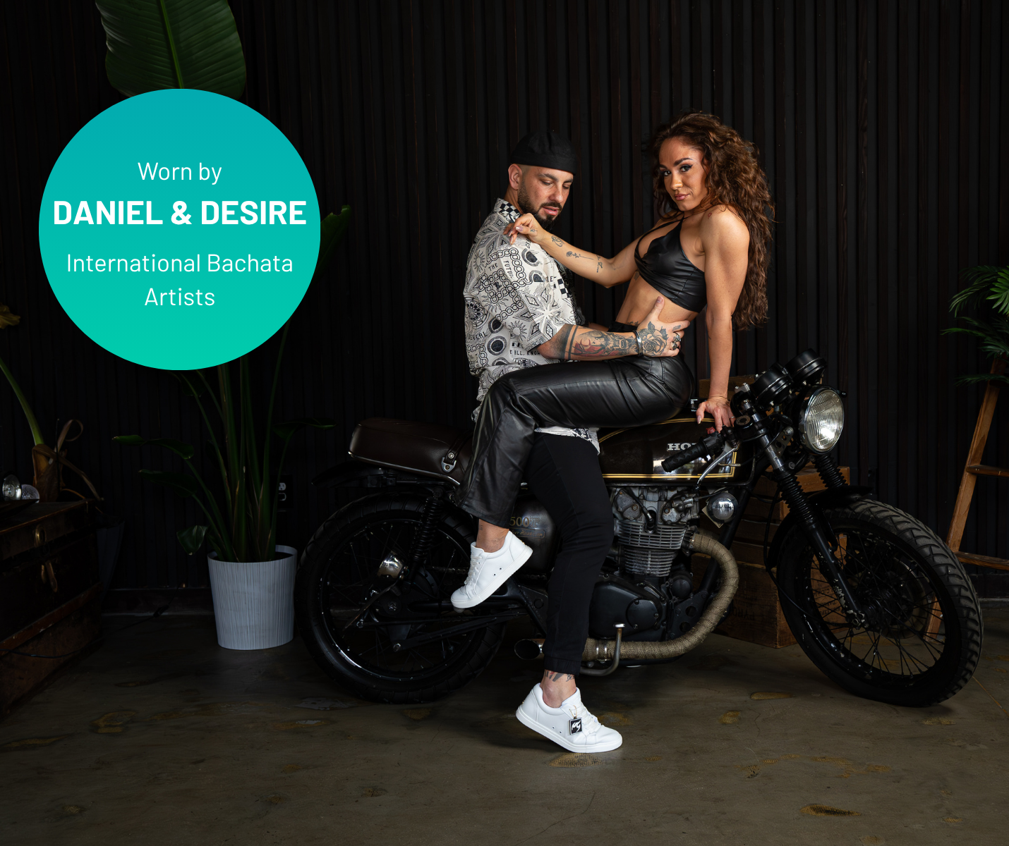 Ein Mann und eine Frau posieren auf einem Motorrad; der Text lautet: „Getragen von Daniel & Desire: Fuego Low-Top-Tanzsneaker in Rosa“.