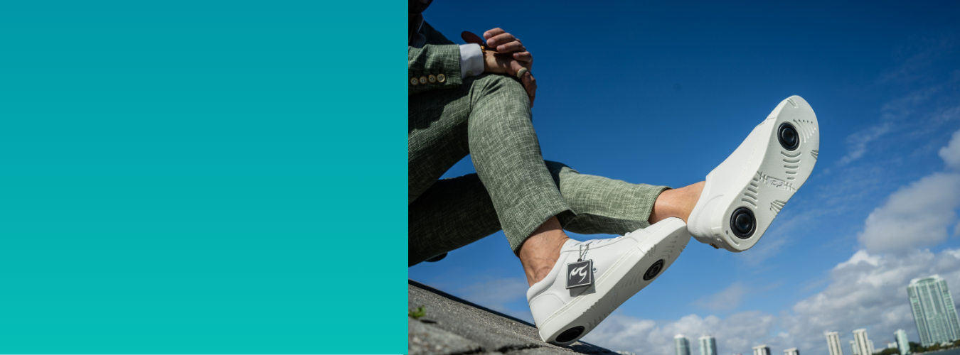 Person in grüner Hose, die im Freien sitzt und weiße Schuhe mit kreisförmigen schwarzen Mustern auf den Sohlen trägt.