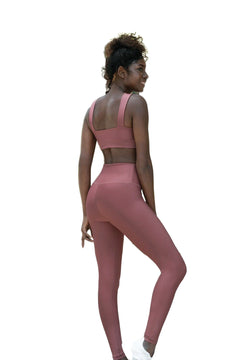 Frau in hoch taillierten Leggings „Lismina Dark Rosé“ und rosa Sport-BH, lächelt über ihre Schulter auf weißem Hintergrund.