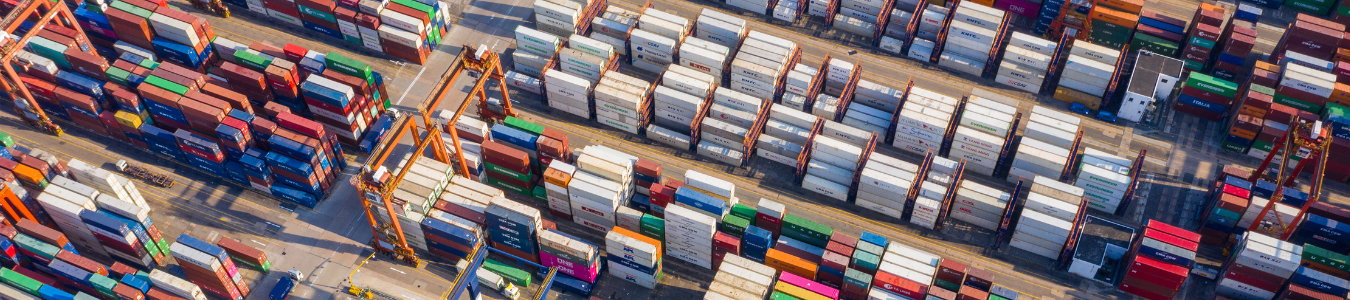 Luftaufnahme von gestapelten Schiffscontainern in einem belebten Hafenlogistikgelände.