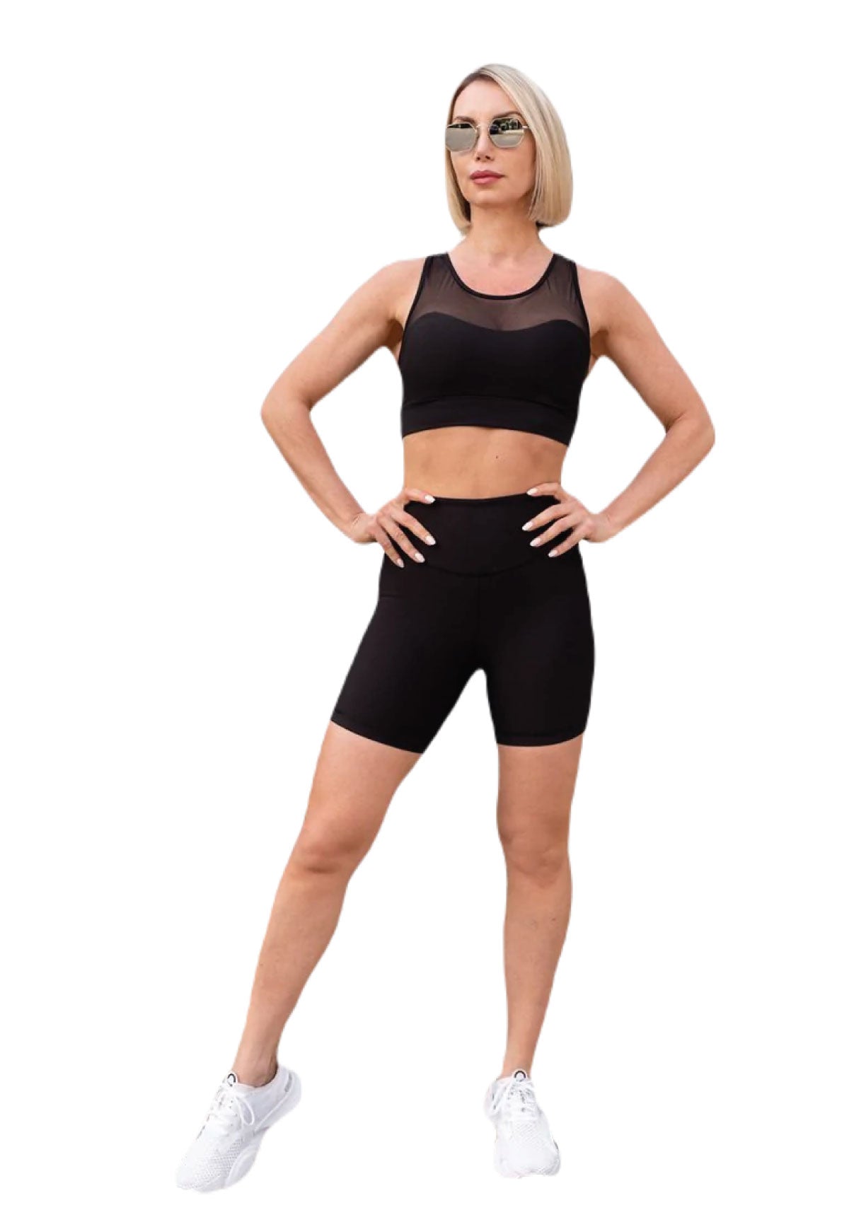 Die Person in Lisminas 7001 Midi Short in Schwarz und weißen Sneakers steht selbstbewusst mit den Händen in den Hüften.