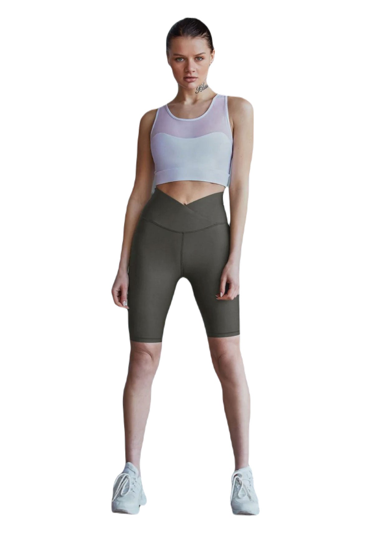 Eine Person in einem Lismina 203 Sport Bra Tulle Detailed in Weiss, dunklen Radlerhosen und weißen Sneakers steht auf einem weißen Hintergrund.