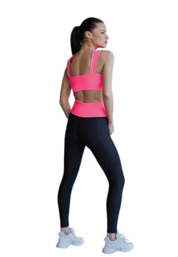 Frau im Lismina 193 Decoltée Sport-BH in rosa und schwarzen Leggings, Hände auf den Hüften, abgewandt, weißer Hintergrund.