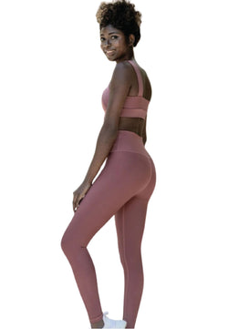 Frau lächelt in Lisminas Dark Rose 1100 Ve Waist Leggings, lockigem Haar und weißen Turnschuhen auf weißem Hintergrund.