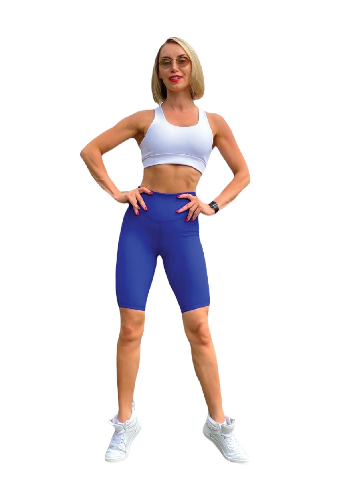 Person, die selbstbewusst in einem Lismina 102 Single Crossed Sport Bra in Weiss und blauen Shorts mit weißen Sneakers posiert.