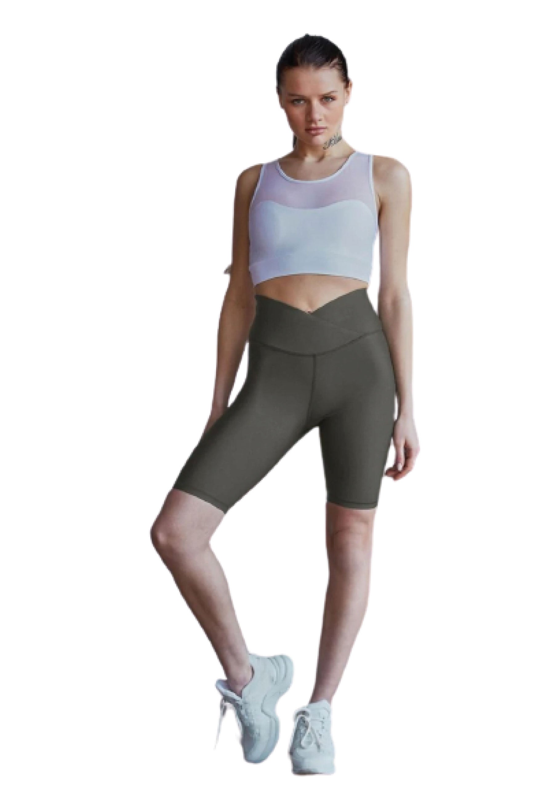 Frau in einem Lismina 203 Sport-BH mit Tülldetails in Weiss und dunklen Radlerhosen, posiert mit angewinkelten Beinen und weißen Sneakers.