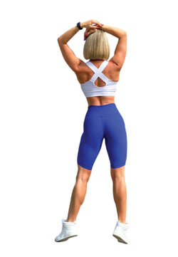 Eine Person in einem Lismina 102 Single Crossed Sport-BH in Weiss und blauen Shorts, die sich vor einem weißen Hintergrund streckt.
