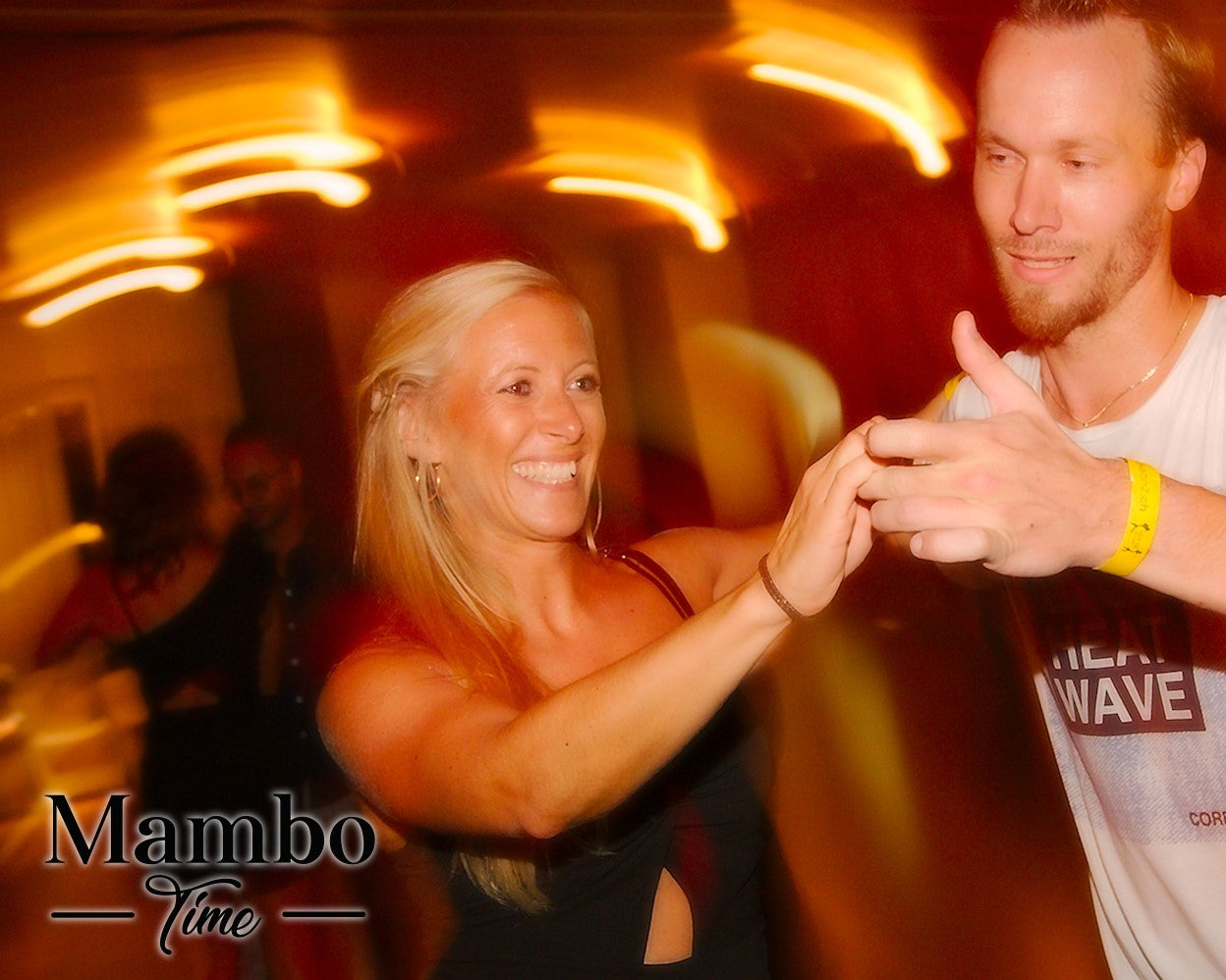 Eine lächelnde Frau und ein lächelnder Mann tanzen zusammen unter warmen, verschwommenen Lichtern mit dem Text Mambo Time in der Ecke.
