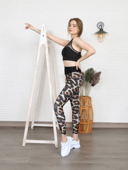 Frau in Lisminas 1080 Extra High Waist Leopard Leggings posiert neben einer Holzleiter mit einer Korbvase und einer Lampe.