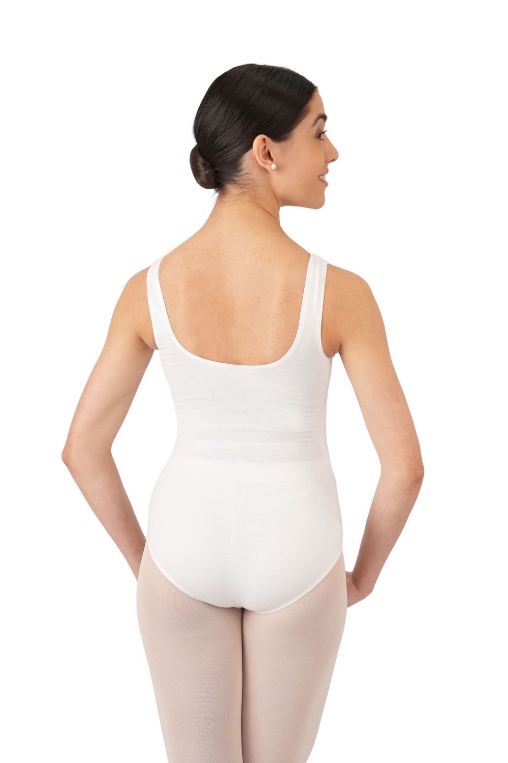 Eine Tänzerin in Rumpfs ärmellosem Body R3101 Weiss steht mit abgewandtem Gesicht da, die Hände in die Hüften gestemmt, das Haar zu einem Dutt gebunden.