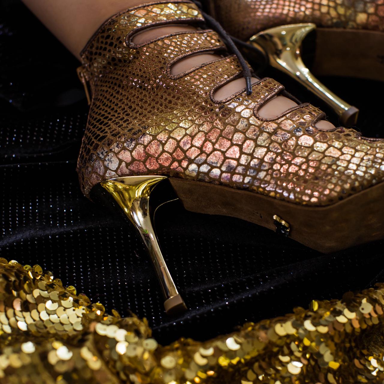 Bronzefarbene Piton-Absätze „Electra“ von Dancing Queens auf schwarzem Stoffhintergrund mit Pailletten.