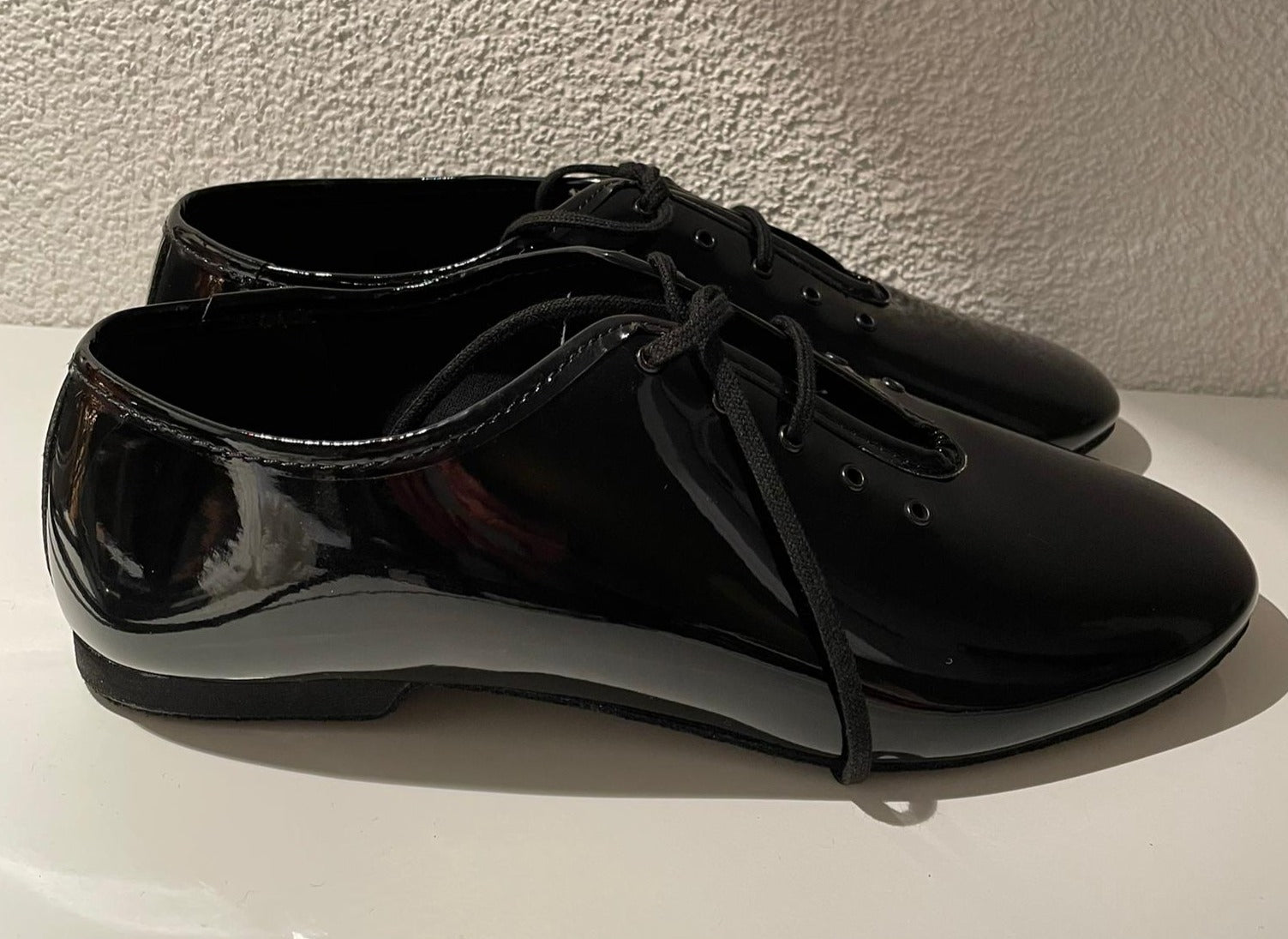 Lidmag 550/J03 Tanzschuhe aus schwarzem Lackleder mit Schnürung auf weißem Untergrund, vor einer strukturierten Wand.