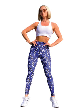 Eine Person in einem weißen bauchfreien Top, blau-weiß gemusterten Leggings mit hoher Taille von Lismina und einer Sonnenbrille steht selbstbewusst da.