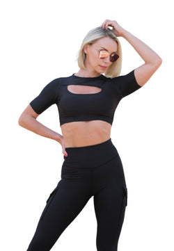 Person in Lisminas 073 T-Shirt in Schwarz und Sonnenbrille posiert selbstbewusst und verströmt mit einem erhobenen Arm verführerisches Flair.